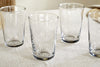 The nkuku Pani Highball - Clear (Set of 4) features elegant recycled glass tumblers, beautifully arranged on a textured tablecloth in soft natural light—ideal for stylish everyday dining.