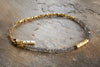 The Perdu Labradorite Bracelet - Gold by nkuku features delicate gray labradorite beads, textured gold brass beads, and a gold chain clasp with a rectangular tag engraved nkuku. Ideal for natural stone jewelry lovers. Displayed on a stone surface.