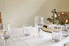 A simple dining table set for everyday use, featuring nkukus Pani Wine Glasses (Set of 4), a small vase with eucalyptus branches, woven placemats, and neutral napkins on a light tablecloth.