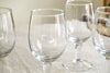 The nkuku Pani Wine Glass - Clear (Set of 4) features durable, recycled glassware arranged on a light tablecloth with soft lighting and a softly blurred background—perfect for elevating everyday dining.