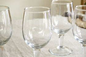 The nkuku Pani Wine Glass - Clear (Set of 4) features durable, recycled glassware arranged on a light tablecloth with soft lighting and a softly blurred background—perfect for elevating everyday dining.