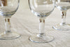 The nkuku Pani Wine Glass - Clear (Set of 4) features sturdy, recycled glass with wide stems, arranged closely on a light cloth—ideal for everyday dining.