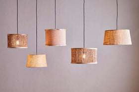 Five nkuku Dia Jute Lampshade - Natural pendant lamps hang against a plain, light wall. Each showcases unique woven or jute styles and shapes, adding warm ambient light and textured, cozy charm to modern décor.