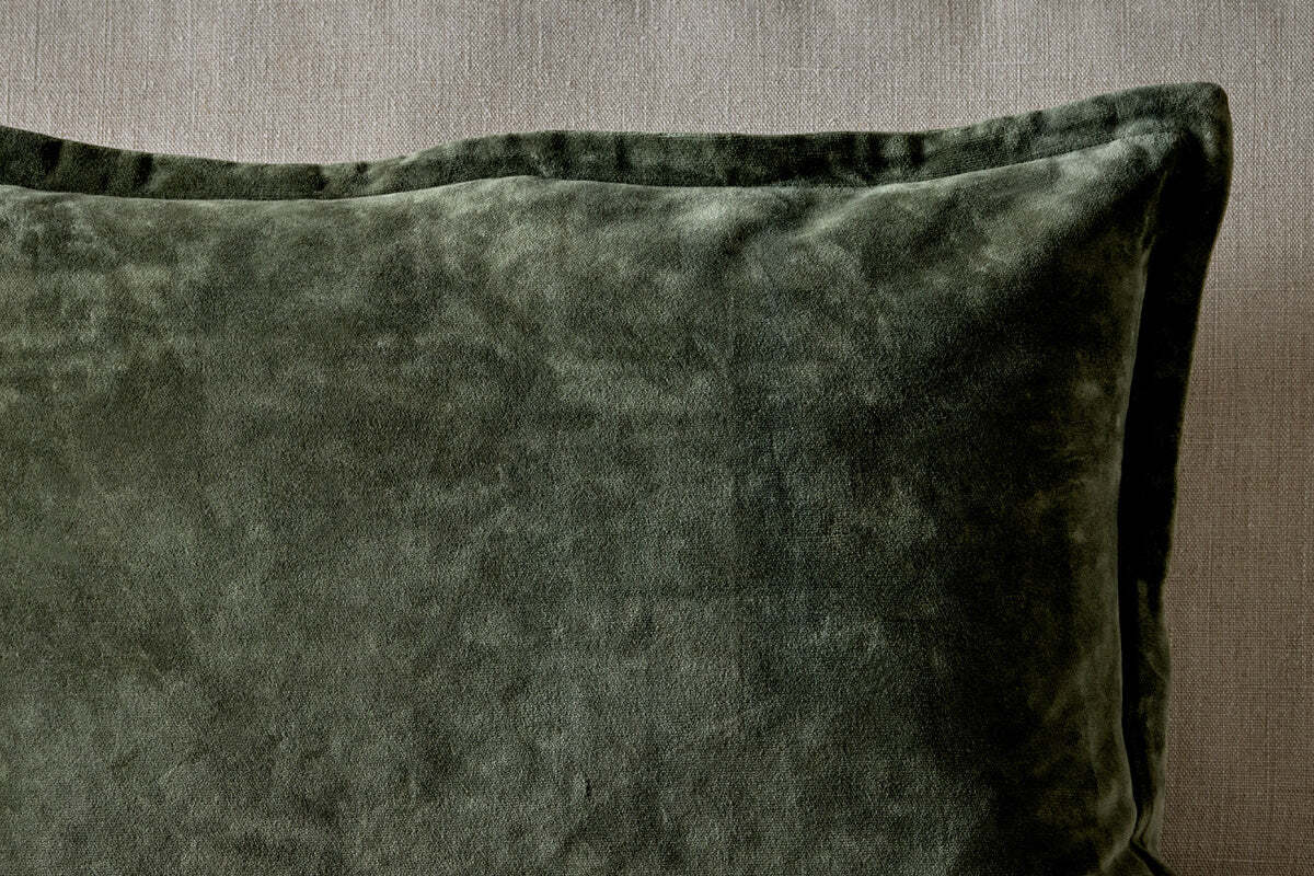 A close-up of the nkuku Pilani Velvet & Linen Cushion Cover in Moss, highlighting its deep green velvet against a textured linen backdrop.