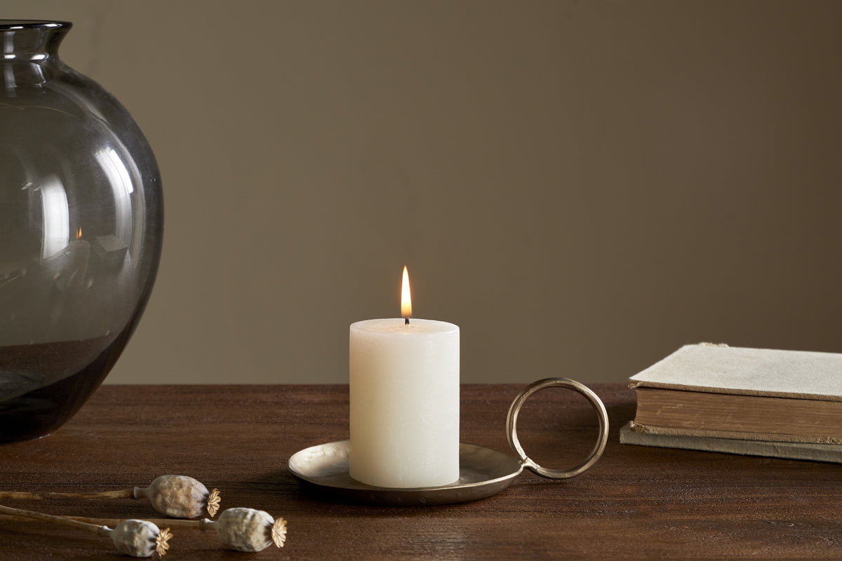 The Rustic Soy Blend Mini Pillar Candle - White by nkuku features a textured finish and sits elegantly on the table, adding charm to any setting.