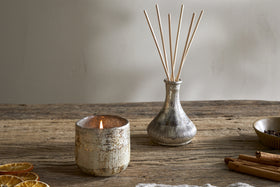 A cozy display featuring nkukus Mandarin & Clove 1 Wick Scented Candle in a textured holder, paired with a small reed diffuser vase, dried orange slices, and cinnamon sticks for festive charm.