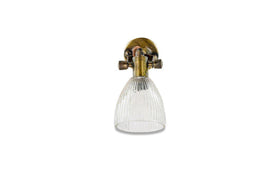 The nkuku Rarni Recycled Glass Single Wall Light features a vintage-style brass fixture and an oval mount that supports a downward-facing, ribbed clear glass shade, blending classic charm with sustainable materials.