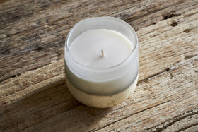 A nkuku Cardamom & Amber 1 Wick Scented Candle in a frosted glass container rests on a rustic wooden surface, its centered wick still unused.