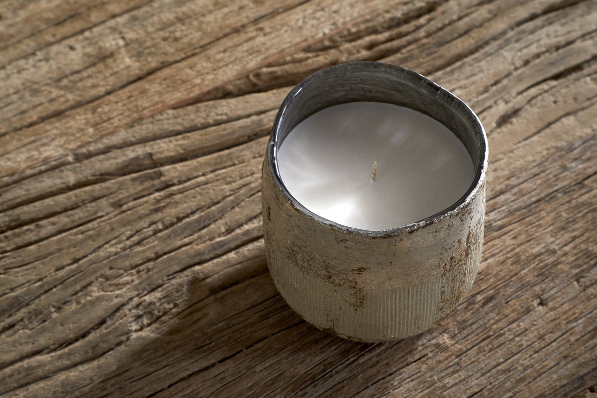 The nkuku Mandarin & Clove 1 Wick Scented Candle, in a rustic weathered metal container, sits on a textured wooden surface with visible grain patterns.
