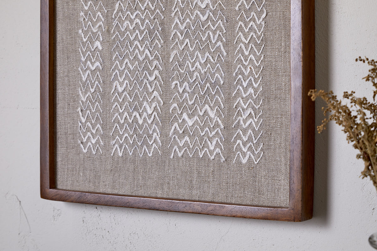 The Samaya Hand Stitched Wall Art - Natural by nkuku features white zigzag embroidery on beige linen, framed in warm brown sustainable mango wood—an elegant accent for your wall décor.