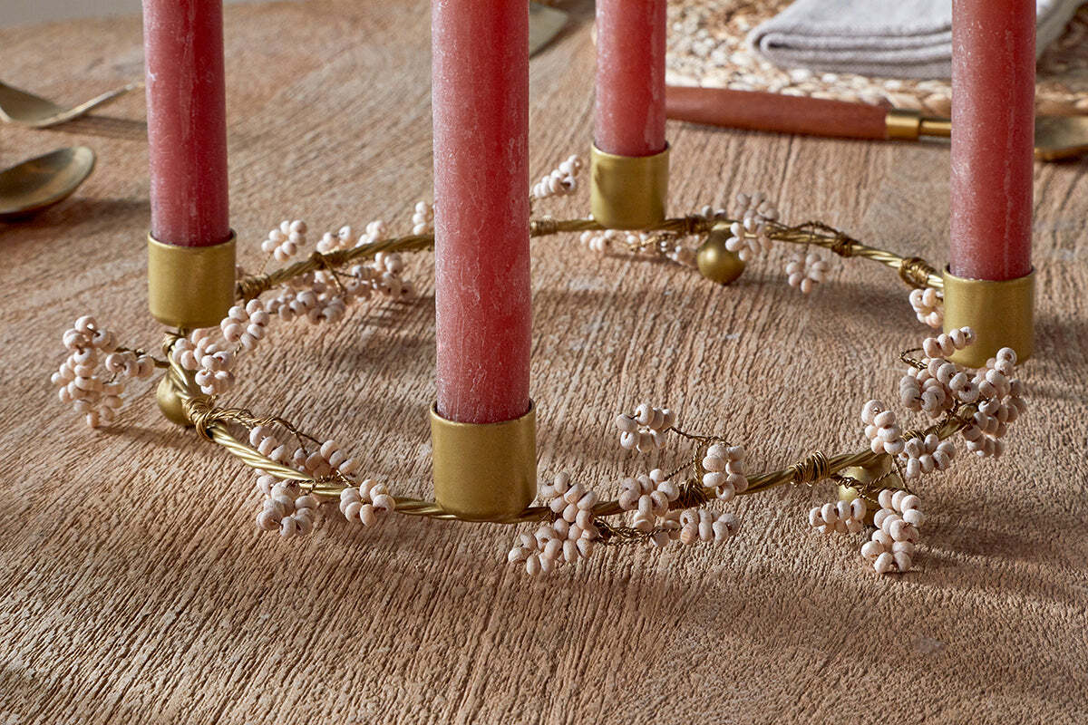 The nkuku Tanu Mango Wood Beaded Candle Holder in brass and natural features four red candles with delicate white berry clusters, creating an elegant, rustic centerpiece ideal for festive tablescapes.