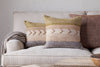 A couch with pillows featuring nkuku’s Tuleeka Wool Cushion Cover in ochre, showcasing a textured woven design.