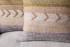 The Tuleeka Wool Cushion Cover - Ochre by nkuku features a stylish textured woven design with beige, peach, gray, and olive stripes and raised chevron patterns, enhancing any light gray fabric surface.