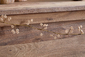 The Tanu Mango Wood Beaded Garland by nkuku features natural wood beads and brass accents, elegantly draped on a surface to showcase its delicate craftsmanship and warm, earthy tones.