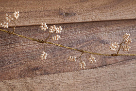The nkuku Tanu Mango Wood Beaded Garland features natural and brass beads strung along a delicate wire, resembling festive clusters. Displayed on rustic wooden planks, it adds an elegant, handcrafted touch to your decor.