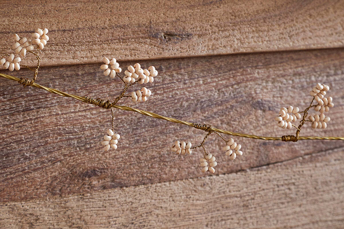 The nkuku Tanu Mango Wood Beaded Garland features natural and brass beads strung along a delicate wire, resembling festive clusters. Displayed on rustic wooden planks, it adds an elegant, handcrafted touch to your decor.