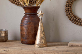 The Talna Tree Bell - Antique Brass by nkuku, a gold cone-shaped piece reminiscent of an antique brass bell, sits beside a vase.