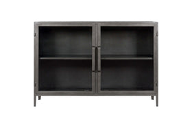 The Takua Iron Sideboard by nkuku features a black metal frame, two glass front doors with slim vertical handles, and four slender legs. Inside, a central shelf divides the storage space. Its minimalist style draws on strong industrial design influences.