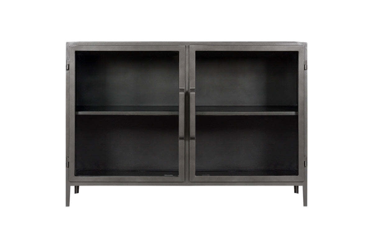 The Takua Iron Sideboard by nkuku features a black metal frame, two glass front doors with slim vertical handles, and four slender legs. Inside, a central shelf divides the storage space. Its minimalist style draws on strong industrial design influences.