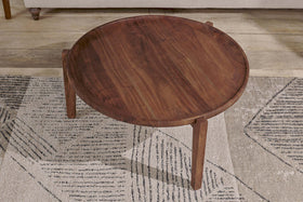 The nkuku Umar Mango Wood Coffee Table in dark brown, featuring a circular shape and tapered legs, sits on a rug with black and beige geometric patterns.