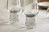A set of four nkuku Visla Champagne Flute - Clear glasses with thick bases are placed upside down on a light-colored, textured tablecloth, with part of a white plate visible in the background.