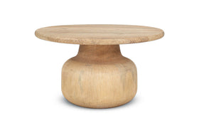 The nkuku Vivan Grooved Wood Coffee Table features a wide top and thick curved pedestal base in sustainable mango wood. With a light natural finish and visible grain, it offers contemporary style against a white background.