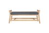 The Avanthi Upholstered Sleigh Bench by nkuku features a simple, modern design with angled legs, vertical slat sides, an elegant carved frame in natural wood finish, and a charcoal gray upholstered cushion seat.