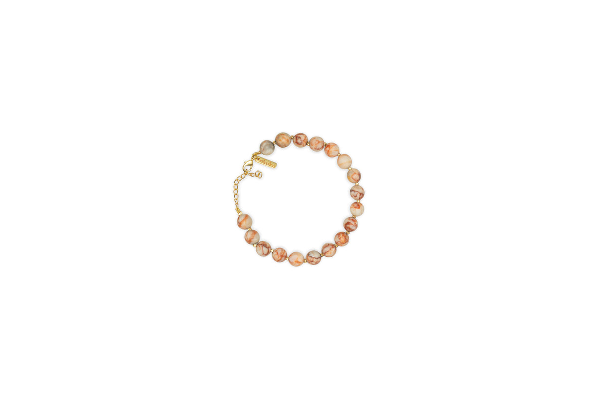 The nkuku Cerita Bracelet - Rhodochrosite showcases round marbled pink and beige stones, strung together with a gold chain extender and clasp. Presented on a plain white background, it’s a versatile accessory.
