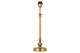 The Ehadi Antique Table Lamp by nkuku features a tall, slender antique brass base with decorative detailing and a round pedestal, shown without shade or bulb, set against a white background.