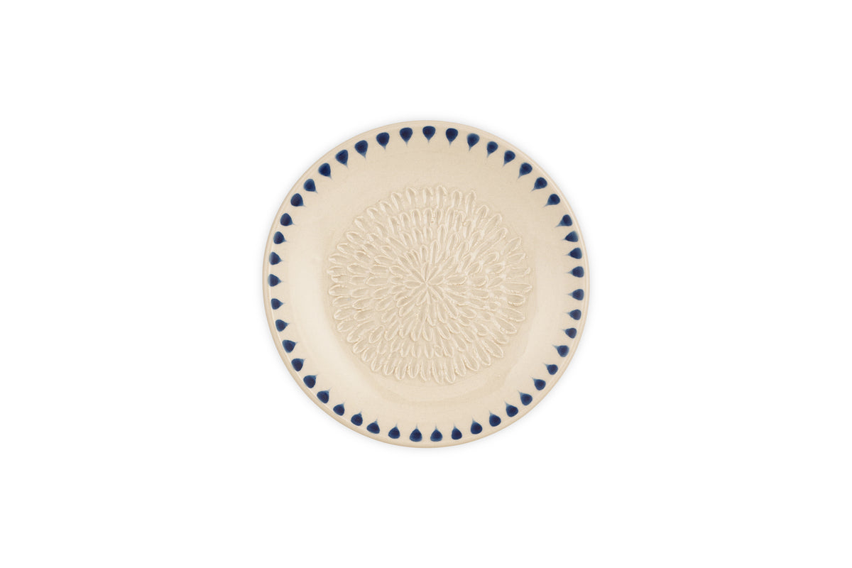 The nkuku Indigo Drop Garlic Grater in cream and indigo features an intricate raised looped center pattern and a border of blue teardrop shapes, with a subtle hand-painted design from the Indigo Drop collection.