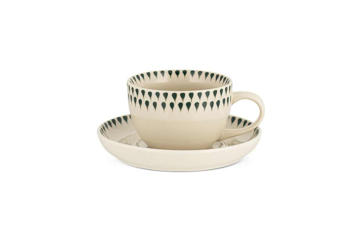 The nkuku Juniper Drop Cup & Saucer in Cream & Juniper features a cream ceramic cup with a handle and green drop detail by the rim, paired with a matching saucer—ideal for elevating any tea or coffee setting.