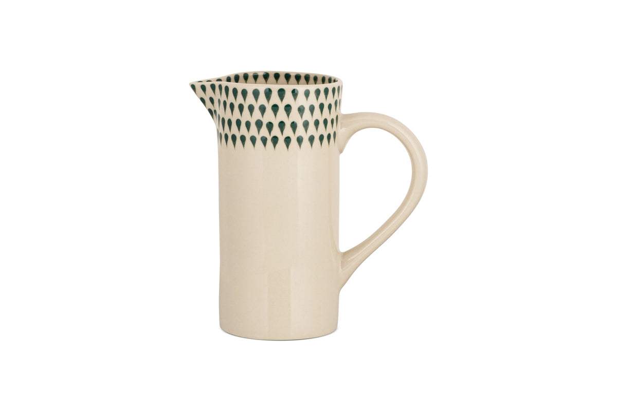 The Juniper Drop Jug - Cream & Juniper - Small by nkuku features a cream ceramic body, curved handle, and narrow spout. Its upper rim is adorned with dark green teardrop patterns—ideal for contemporary tableware collections.