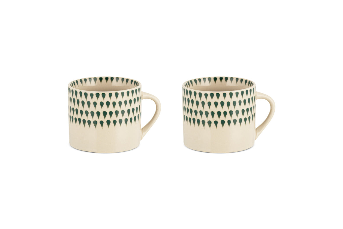 The nkuku Juniper Drop Mug - Cream & Juniper - Small (Set of 2) features two cream ceramic mugs with unique handles and juniper green drop details, displayed side by side on a white background.