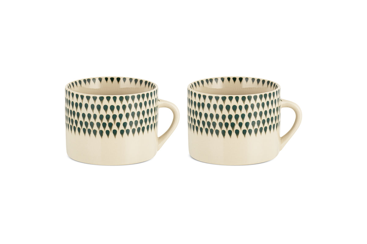 The nkuku Juniper Drop Mug - Cream & Juniper - Large (Set of 2) features two cream ceramic mugs with distinctive handles and a dark juniper green drop design near the rim, shown side by side on a white background.