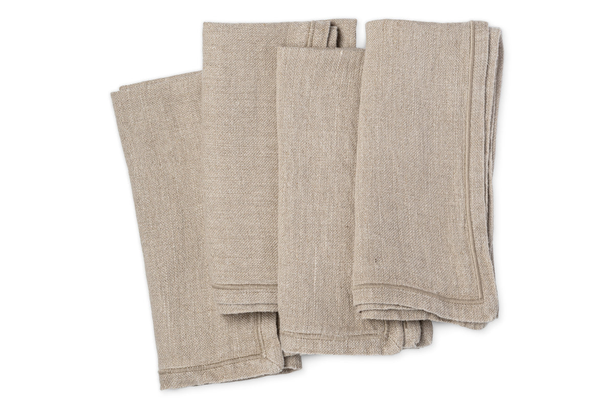 The nkuku Junto Linen Napkin - Natural (Set of 4) features four neatly folded beige linen napkins stacked against a white background, showcasing the fabrics visible texture.