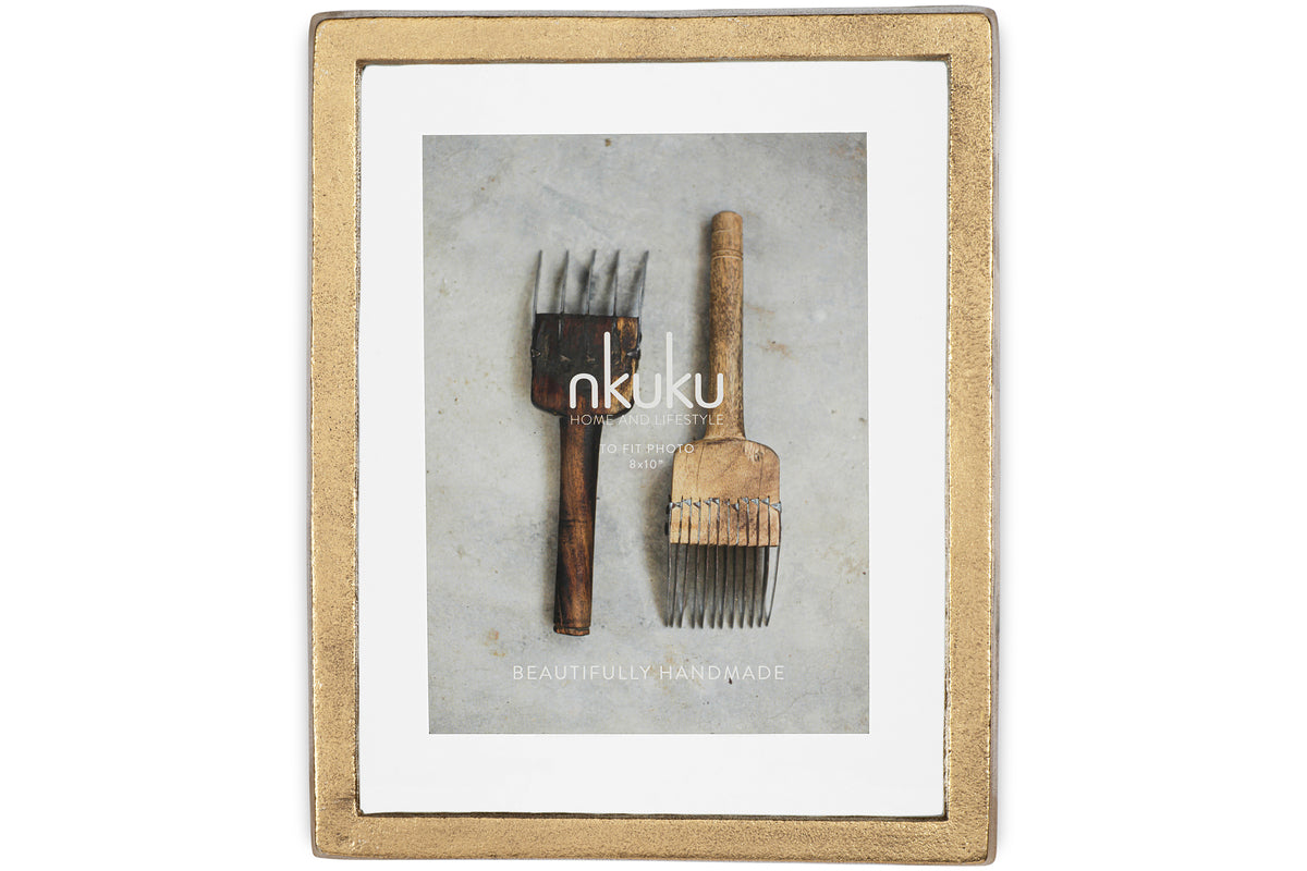 The Jahala Wall Hung Photo Frame in Antique Brass by nkuku displays a photo of two rustic, vintage wooden hair picks on a gray surface, with Beautifully Handmade and Home & Lifestyle overlaid on the image.