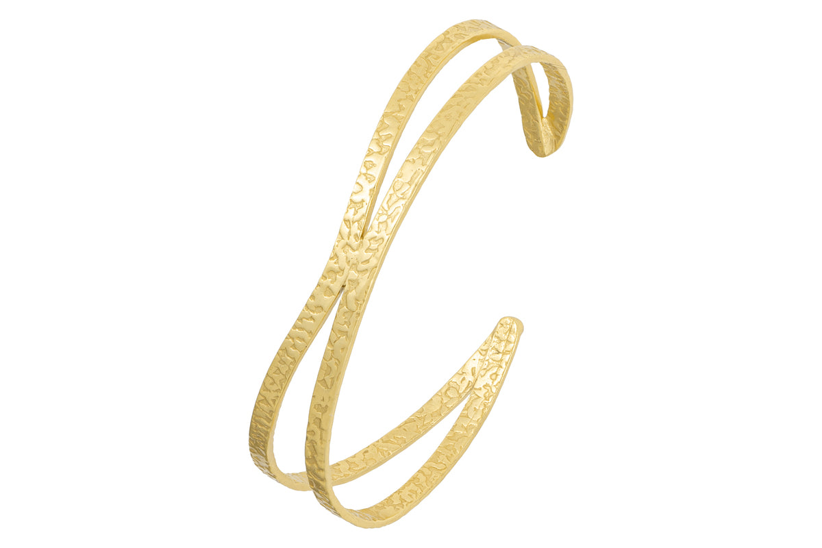 The Katai Bangle - Gold by nkuku is a slim, sculptural gold cuff with a hammered finish and an open-ended, double band design, shown against a white background.