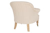 The Kiana Cotton Armchair - Natural by nkuku is shown from the back at an angle on a white background. This beige cotton upholstered chair features hand-carved mango wood legs, with one front leg finished with a brass caster wheel.