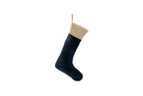 A single nkuku Karru Cotton Velvet Stocking - Indigo hangs side-on. Made from dark blue cotton velvet with a beige textured cuff and loop, it’s ideal for a festive fireplace against a plain white backdrop.