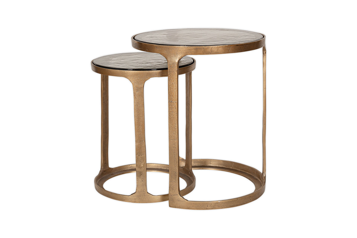 The Khidki Cast Metal & Glass Nesting Side Tables by nkuku feature two round tables with antique brass frames and glass tops, adding elegance to any space.