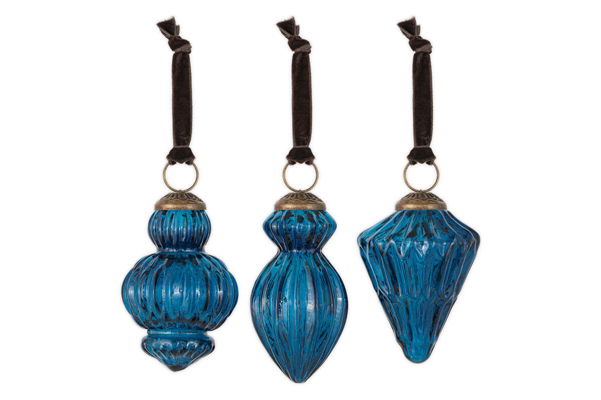 The nkuku Manipur Baubles - Indigo (Set of 3) feature uniquely shaped blue glass ornaments with ribbed textures, vintage silver tops, and brown velvet ribbons—elegant, antique-finished festive decor inspired by classic Christmas styles.