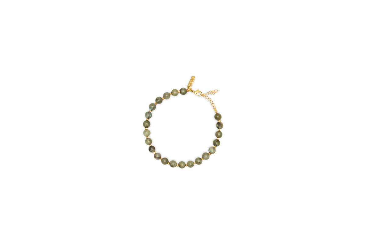 The Marai Bracelet - Labradorite by nkuku features round greenish-brown labradorite beads, a gold clasp, and an adjustable chain. This elegant piece is perfect for jewellery lovers and is presented on a plain white background.