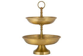 The Mahika Stand - Antique Brass by nkuku is a two-tiered gold metal stand with textured bowls and a top handle, ideal as a centrepiece for festive tablescapes or for displaying fruits, desserts, or snacks.