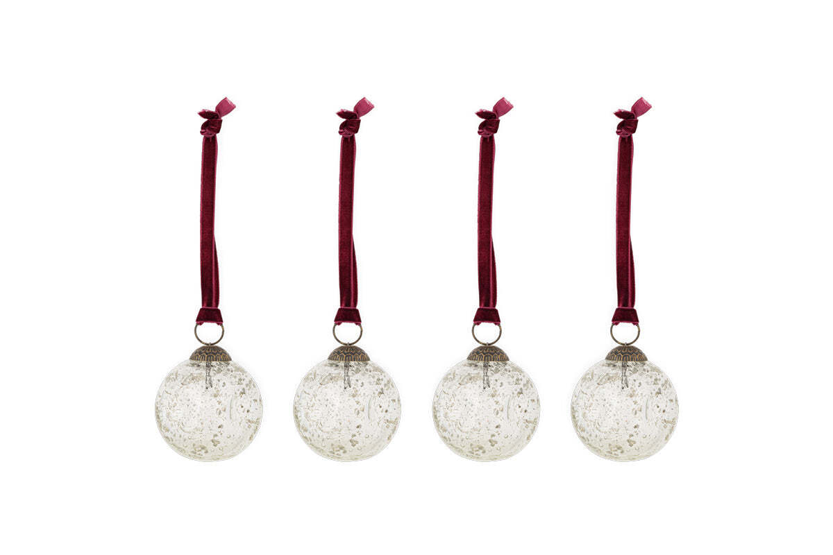 The nkuku Nishan Pinched Baubles - Clear (Set of 4) feature round, recycled glass ornaments with silver caps and burgundy velvet bows, offering a speckled, vintage look that’s perfect for festive decor.