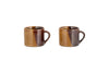 The Naav Mugs - Mustard - Small (Set of 2) by nkuku, each with an angled handle and a glossy mustard and tan color-blocked glaze, are arranged side by side on a white background.