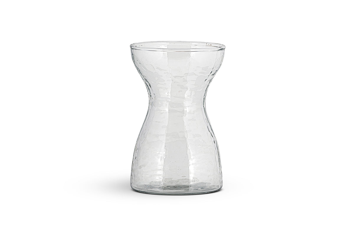 The Enir Hyacinth Vase - Clear by nkuku features clear hammered glass with a textured, dimpled surface and a narrow neck that curves to wide openings. The empty vase is shown against a plain white background.