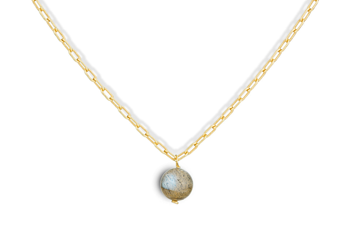 The Marai Labradorite Necklace by nkuku features a gold chain with elongated links and a central round labradorite pendant, displaying blue and brown flecks—an elegant jewelry gift.