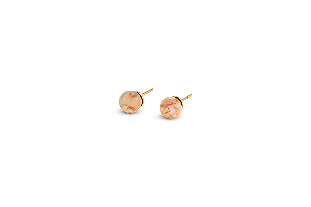 The nkuku Cerita Rhodochrosite Stud Earrings feature round marbled peach and cream rhodochrosite stones in a minimal gold-plated bezel, displayed on a plain white background with ample empty space.