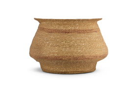 The nkuku Rana Wide Basket - Natural & Rust is an hourglass-shaped, handwoven storage basket in tan and rust tones, featuring a wide mouth, rounded body, and narrow base, crafted from natural seagrass. Shown on a white background.