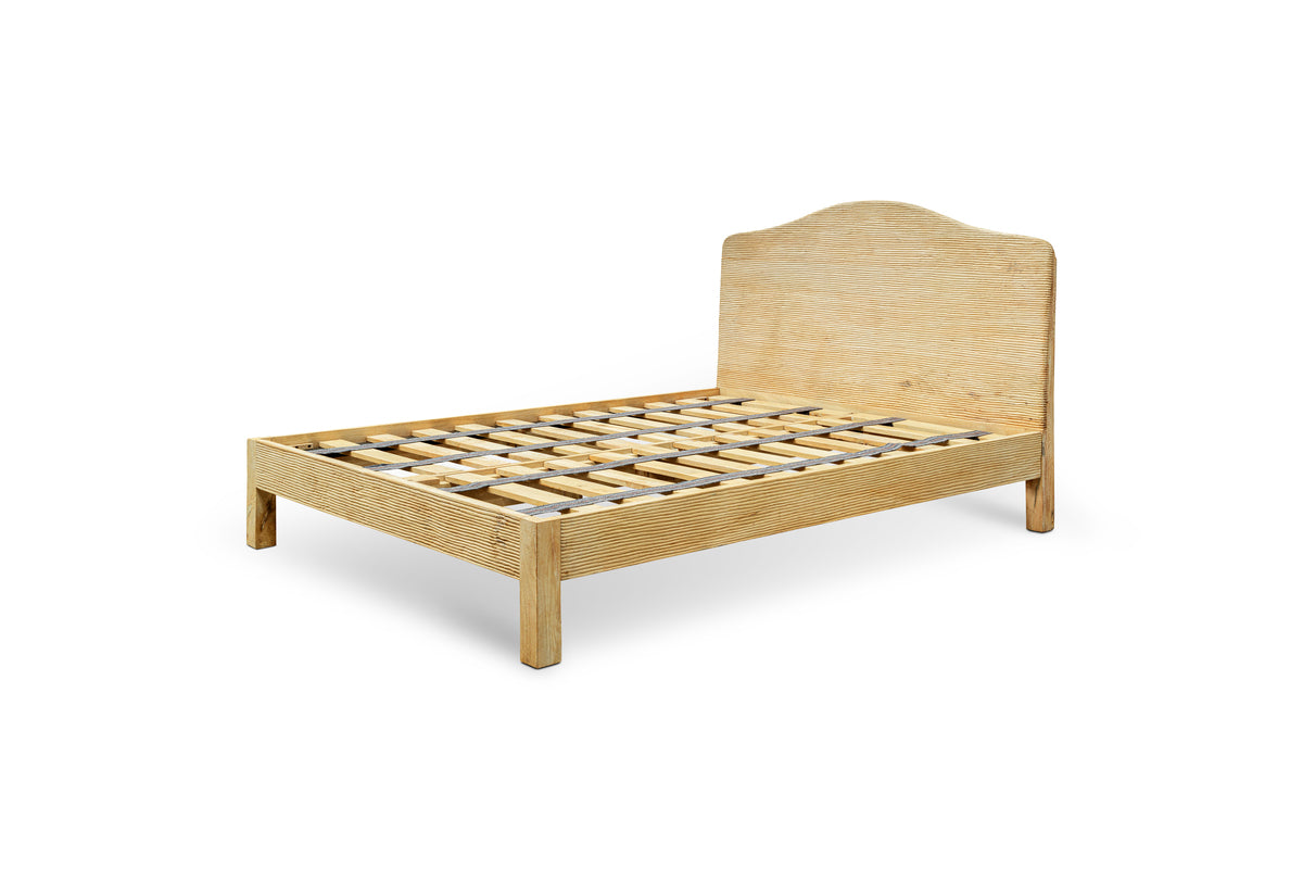 The Vivan Grooved Bed by nkuku features a tall, curved headboard and slatted base. Crafted from light natural wood with textured grain, this sturdy frame stands on four legs and is shown without a mattress or bedding against a white background.